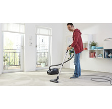 Un bărbat aspiră podeaua într-o cameră luminoasă cu un aspirator.