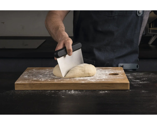 O persoană împarte aluat cu un răzuitor de aluat pe o scândură de lemn.