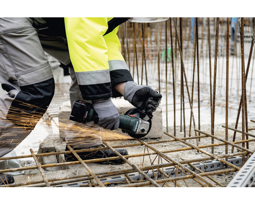 Un muncitor taie bare de armătură cu un polizor unghiular cu acumulator.