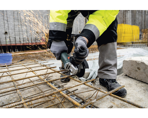 Un bărbat taie oțel de armare cu un polizor unghiular pe un șantier.