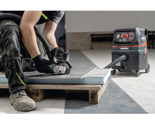 Artizan taie o placă de faianță cu un polizor unghiular, conectat la un aspirator industrial marca Metabo