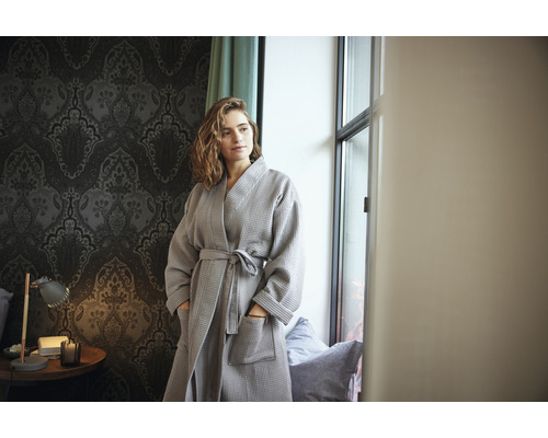 Femeie cu halat de baie gri tip fagure într-o cameră cu tapet cu model