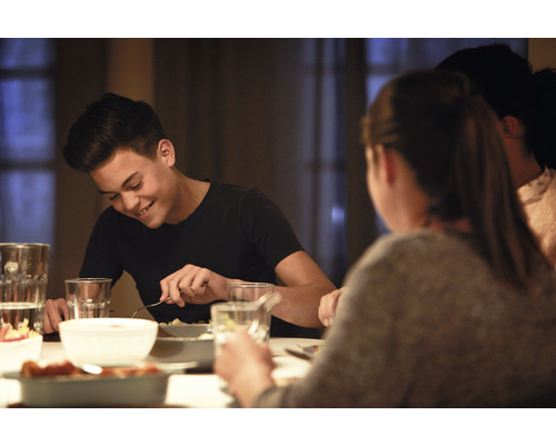 Scenă de cină cu persoane așezate la o masă, savurând mâncare și băuturi.