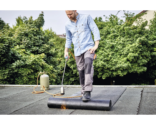 Un bărbat instalează o membrană de acoperiș pe un acoperiș cu o torță de acoperiș.