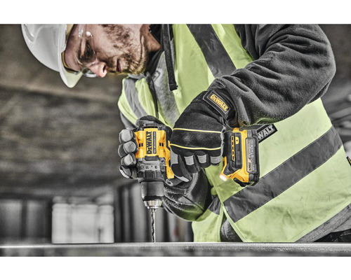 Un muncitor în construcții cu cască de protecție și vestă de siguranță găurește metal cu o bormașină DeWalt.