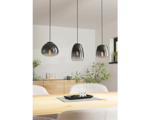 Trei lămpi suspendate gri de diferite forme deasupra unei mese din lemn