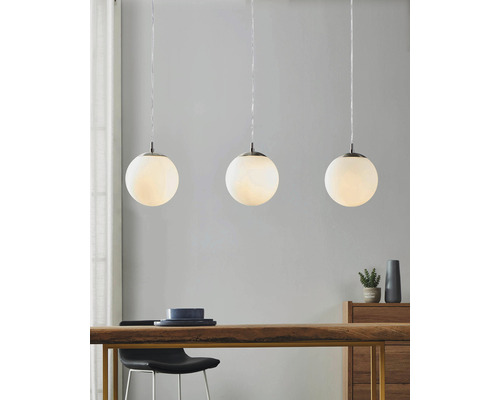 Trei lămpi suspendate cu abajururi rotunde din sticlă albă deasupra unei mese din lemn.