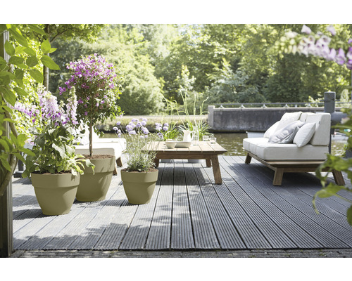 Scenă de grădină cu jardiniere, podea de lemn, canapea și masă pe malul apei
