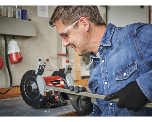 Bărbat șlefuind o tijă metalică cu o mașină de șlefuit dublă Einhell