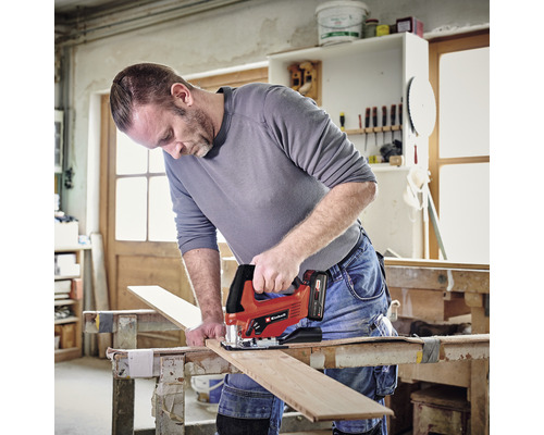 Un bărbat taie o scândură de lemn cu un fierăstrău vertical cu acumulator pe un banc de lucru într-un atelier.
