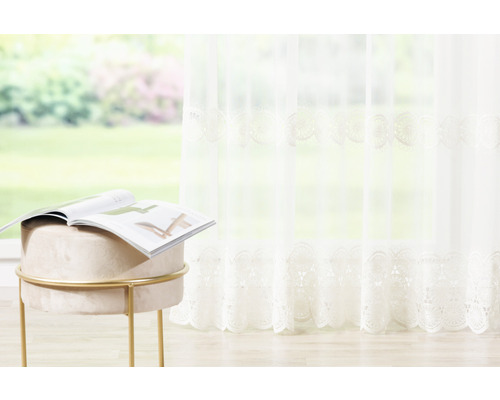 Cortină decorativă, transparentă, cu broderie și un taburet cu o revistă pe el.