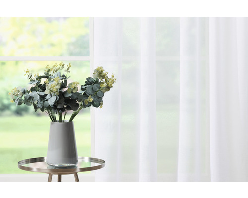 Ramuri decorative de eucalipt într-o vază pe o măsuță laterală în fața unei ferestre cu perdea