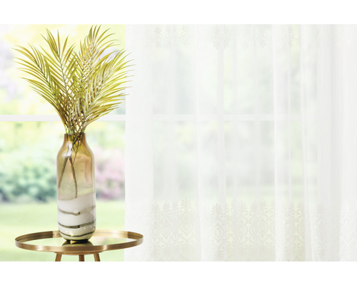 Scenă decorativă cu palmier artificial în vază pe măsuță în fața ferestrei cu perdea