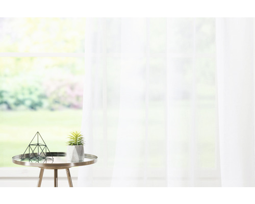 Cortină decorativă, transparentă, în fața unei ferestre, completată de o plantă de interior și un decor geometric pe o măsuță laterală.