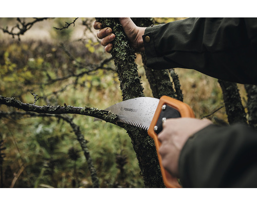 Persoană taie o ramură cu un ferăstrău de ramuri de la Fiskars.