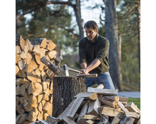 Bărbat taie lemne cu un topor lângă o grămadă de lemne.