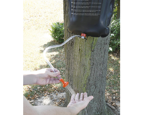 Duș portabil cu picături de apă în mână în fața unui copac