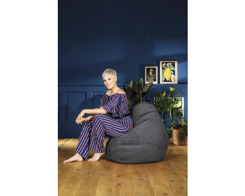 Femeie așezată pe un sac de fasole gri într-o cameră de zi cu plante și decorațiuni