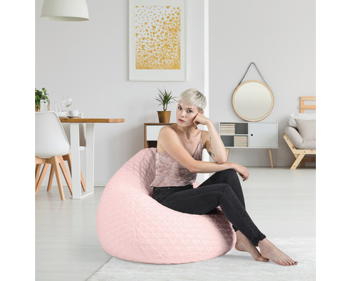 Femeie șezând pe un sac de fasole roz într-o cameră de zi luminoasă.