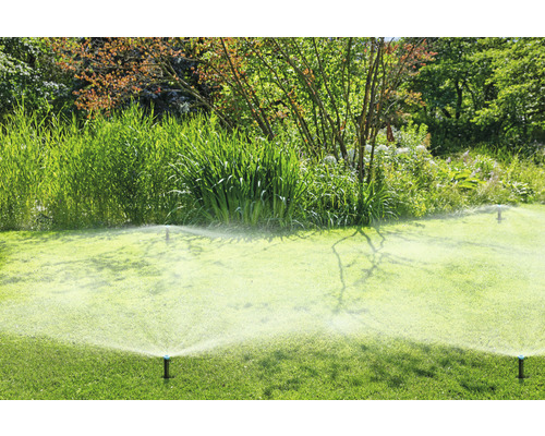 Aspersoare de gazon udând o peluză verde într-o grădină.