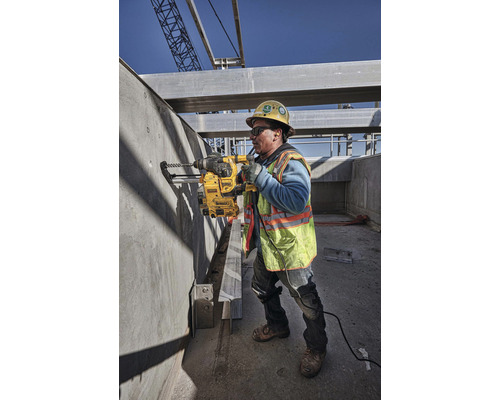 Un muncitor în construcții forează o gaură într-un perete de beton cu o mașină de găurit pe un șantier.