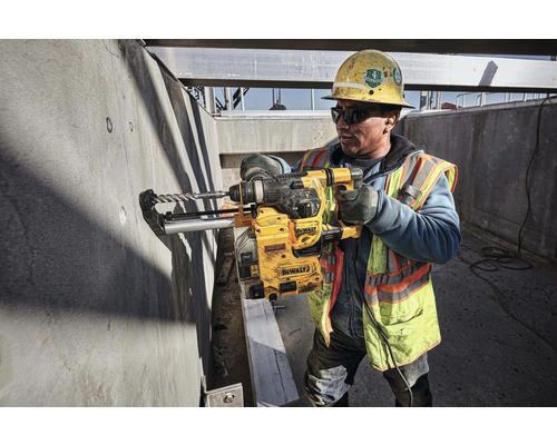 Un muncitor în construcții găurește un zid de beton cu o mașină de găurit DeWalt pe un șantier.