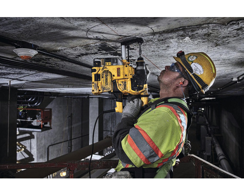 Un muncitor în construcții găurește un tavan de beton cu o carotieră DeWalt.