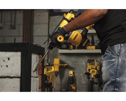 Un bărbat folosește un ciocan rotopercutor DeWalt pentru a găuri un perete de cărămidă.