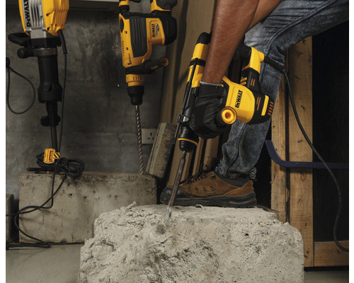 Un meseriaș folosește un ciocan demolator DeWalt pentru a prelucra beton. Alte ciocane rotopercutoare sunt pregătite în fundal.