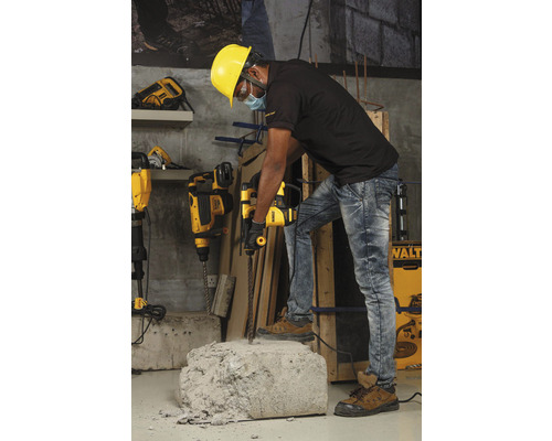 Un muncitor cu cască de protecție folosește un ciocan rotopercutor pentru a lucra o bucată de beton.