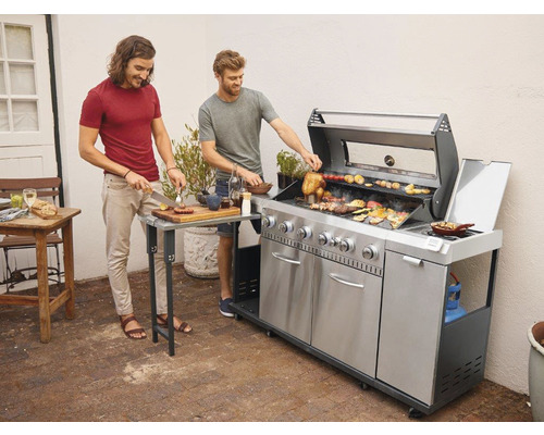 Doi bărbați pregătesc mâncare afară pe un grătar din oțel inoxidabil.