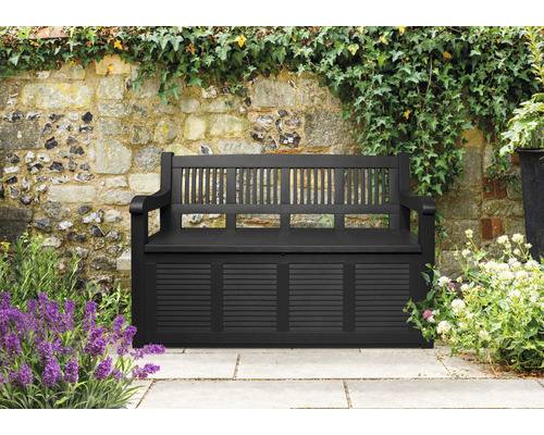 Bancă de grădină cu spațiu de depozitare în fața unui zid de piatră cu plante