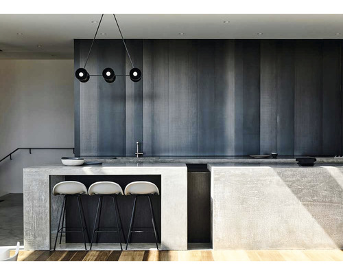 Cameră luminoasă cu insulă de bucătărie din beton, scaune de bar și o lustră modernă