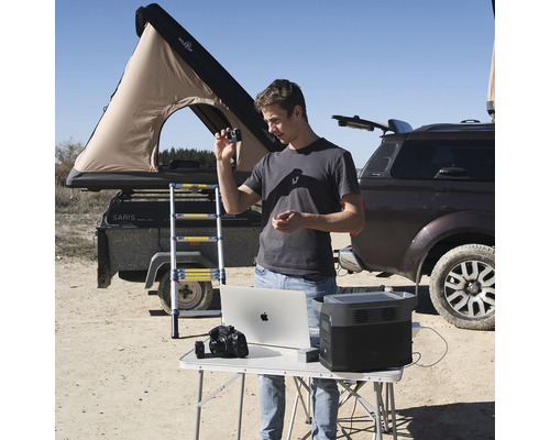 Scenă cu bărbat, laptop, stație de alimentare portabilă, cameră, mașină și cort pe acoperiș pentru excursii de camping în aer liber