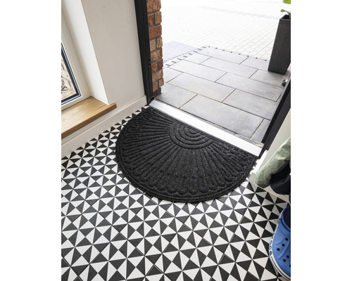 Covoraș semicircular din material textil în fața unei uși de intrare pe o podea cu model geometric