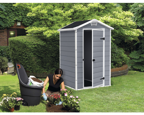 Scenă de grădină cu magazie de scule, roabă și o femeie care plantează flori