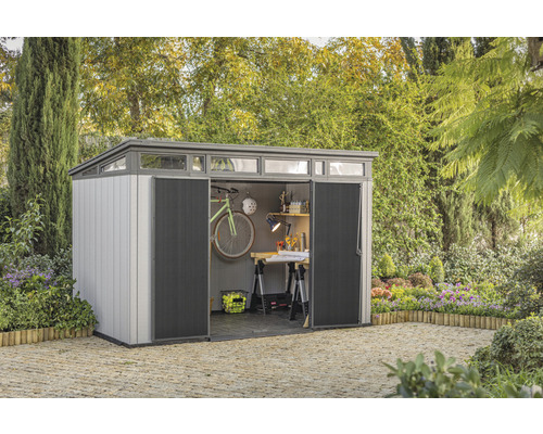 Cabină de grădină cu uși deschise, amplasată în grădină și echipată cu o bicicletă și banc de lucru