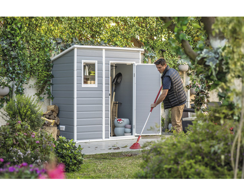 Scenă de grădină cu magazie de scule și bărbat greblând frunze