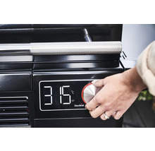 Prim-plan al unui grătar cu afișaj digital al temperaturii, unde o mână acționează butonul