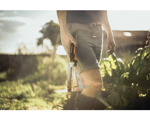 O persoană din grădină ține un dispozitiv de scos buruieni marca Fiskars.