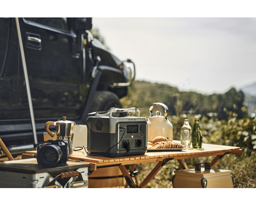 Scenă cu o centrală electrică portabilă Ecoflow, o cafetieră, o cameră foto, o dronă și un ceainic pe o masă de lemn afară