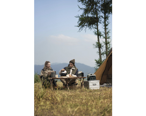 Două persoane în camping cu masă, scaune, ustensile de gătit și cort în natură