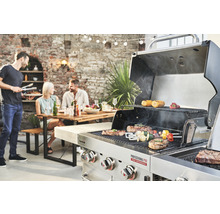 Scenă cu un grătar pe care se prepară fripturi și legume și persoane așezate la o masă