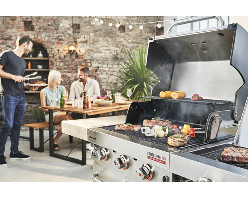 Scenă cu un grătar pe care se prepară fripturi și legume și persoane așezate la o masă