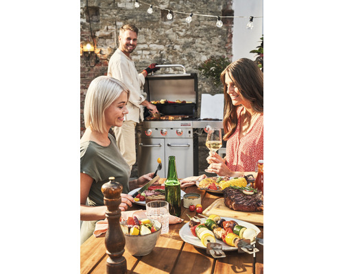 Scenă cu grătar, mâncăruri preparate și trei persoane afară