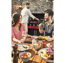 Oameni care fac grătar și mănâncă la o masă de lemn cu un grătar pe gaz în fundal