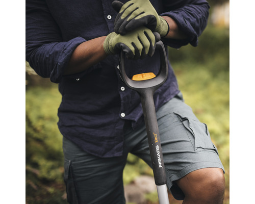 O persoană cu mănuși de grădinărit ține o sapă marca Fiskars.