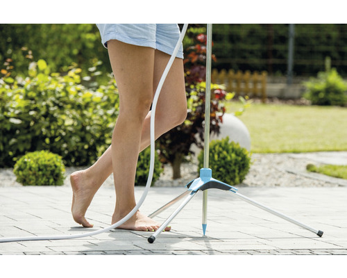 Femeie stă desculță lângă un duș de grădină pe o terasă