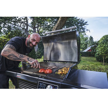 Un bărbat face grătar legume și carne pe un grătar cu cărbune în grădină.