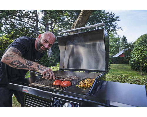 Un bărbat face grătar legume și carne pe un grătar cu cărbune în grădină.